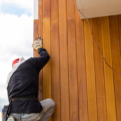 Worker installing siding with a wood grain appearance.